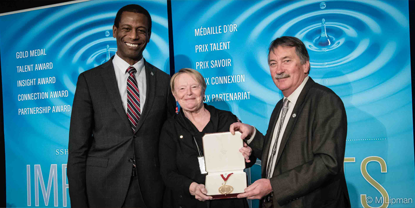 Greg Fergus, Claudia Mitchell holding Gold Medal, and Ted Hewitt
