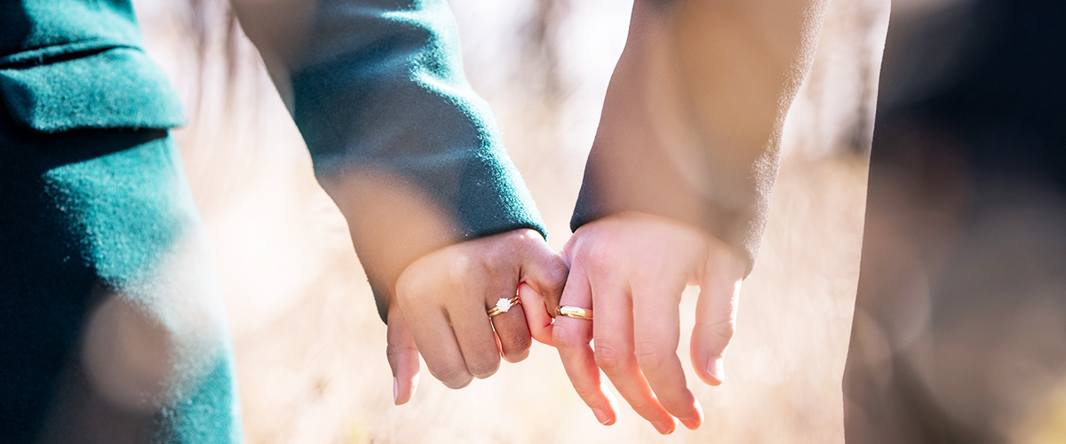 closeup of interracial couple—South Asian and white Canadian— holding hands with their engagement rings