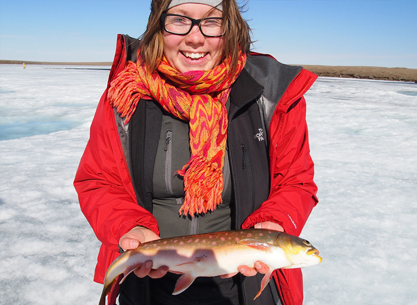 person holding an Arctic char standing on a frozen waterway